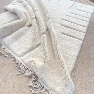 Handwoven cream Moroccan wool rug with modern minimalist textured patterns and fringed edges displayed outdoors